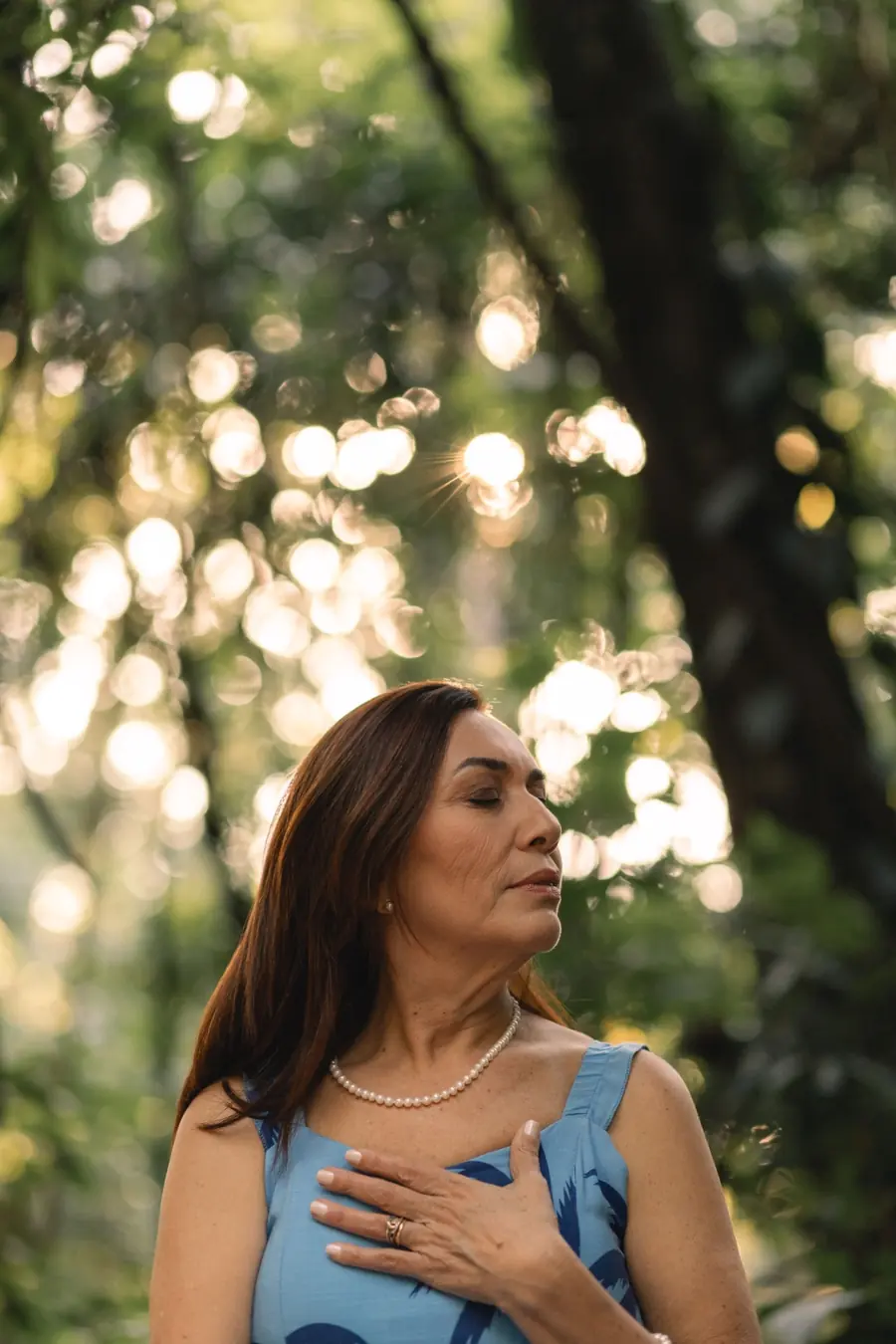 Blácia Gonzales de olhos fechados, com a mão sobre o peito, em meio à natureza
